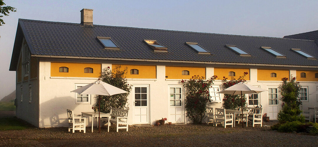 Billede i tåge af den charmerende gårdsplads på Nymarksminde med brostensbelagte stier, blomsterbede og historiske bygninger i baggrunden.